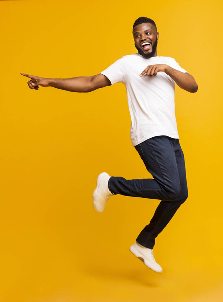 Joyful millennial guy jumping on air and pointing aside - Foto, Imagem