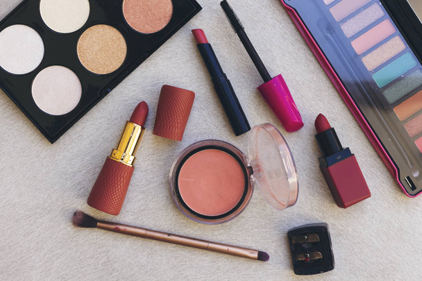 roze blush, diverse lippenstift en lipgloss, mascara brush, oogschaduw en highlighter palet op houten tafel - Foto, afbeelding