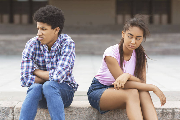 Offended teen couple sitting outdoors, ignoring each other - 写真・画像
