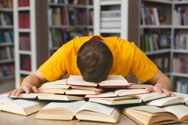 Белый парень дремлет во время учебы в библиотеке
 - Фото, изображение