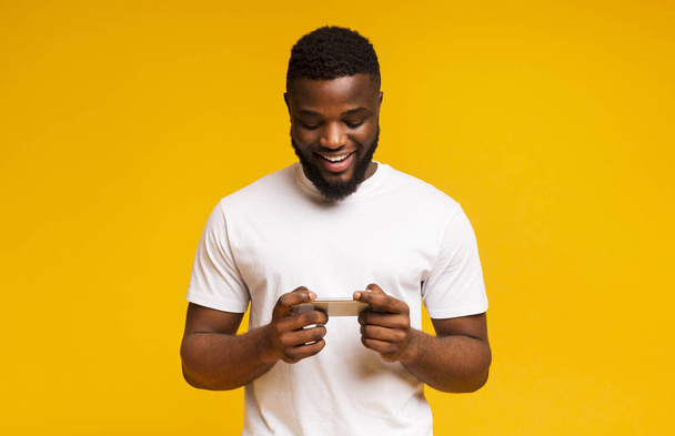 Африканский мужчина играет в видеоигры на мобильном телефоне и улыбается
 - Фото, изображение