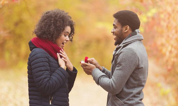 Romantic afro man proposing to woman in autumn park - Photo, Image