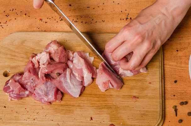 As mãos femininas com uma faca na mão cortam a carne fresca em uma mesa
 - Foto, Imagem