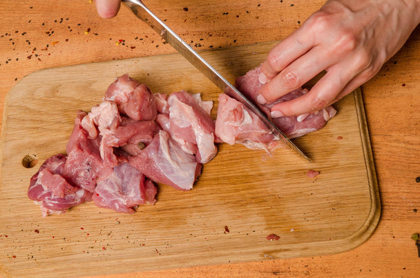 Female hands with a knife in their hand cut fresh meat on a table - Foto, afbeelding