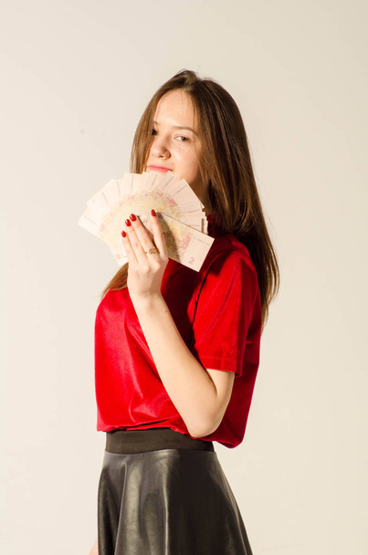 A sexy brunette in a short skirt on a light background counts money. - Photo, Image
