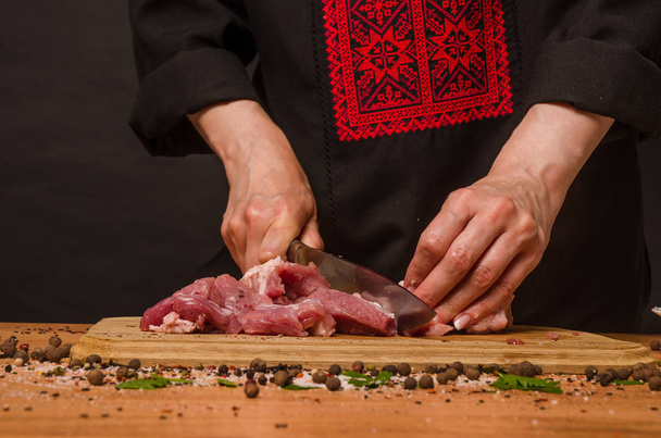 Las manos femeninas con un cuchillo en la mano cortan carne fresca en una mesa
 - Foto, imagen