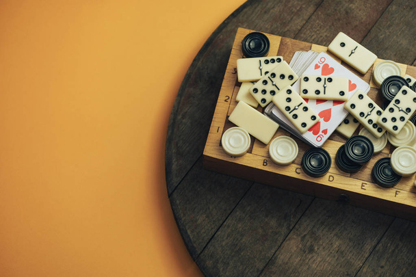 Varios juegos de mesa tablero de ajedrez, jugando a las cartas, dominó sobre una vieja mesa de madera fondo naranja
. - Foto, imagen