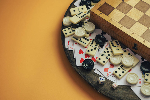 Verschiedene Brettspiele Schachbrett, Spielkarten, Dominosteine auf einem alten Holztisch orangefarbenen Hintergrund. - Foto, Bild