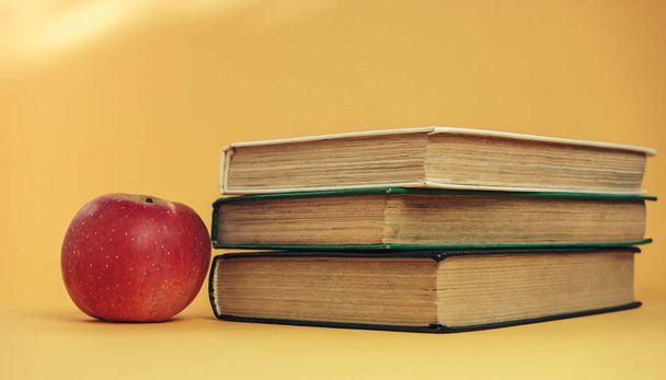 Turuncu arka planda güzel kitaplar ve kırmızı elma.. - Fotoğraf, Görsel