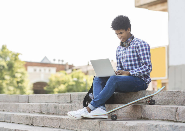 Νεαρός φοιτητής που σπουδάζει σε εξωτερικούς χώρους χρησιμοποιώντας φορητό υπολογιστή - Φωτογραφία, εικόνα