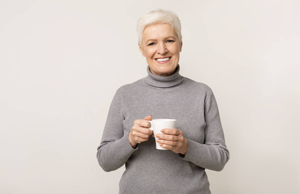 Elderly lady with cup of tea over light studio background - Fotografie, Obrázek