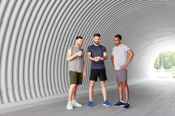 sporty men or friends with smartphone in tunnel - Foto, Imagen