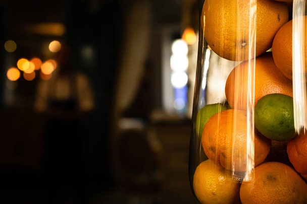 Oranges and lime in a tall glass glass backdrop in warm dark shades blurry. Warm tone. Horizontal orientation. - Photo, image