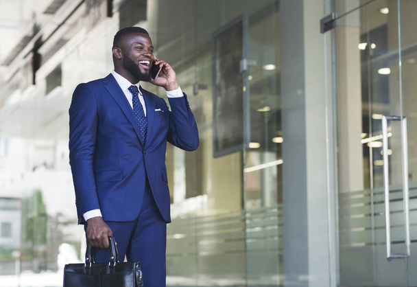 Homme d'affaires joyeux ayant une conversation téléphonique à côté de l'immeuble de bureaux
 - Photo, image