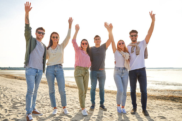 Счастливые друзья размахивают руками на пляже летом
 - Фото, изображение
