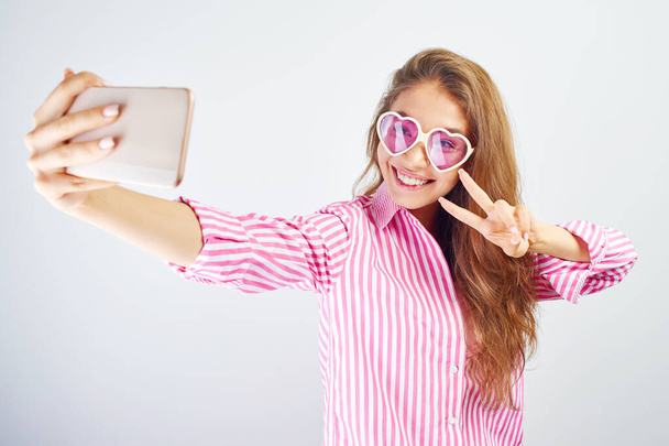 Young funny blogger Asian girlmakes selfie on the phone camera on white background, isolated in studio - Fotoğraf, Görsel