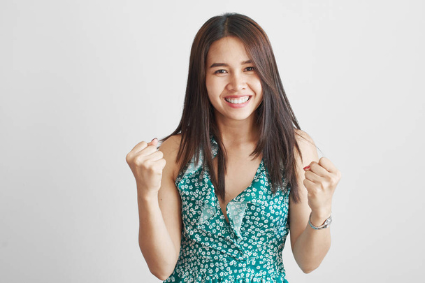 Attractive brunette thai asian girl joyfully clenches fists, celebrates victory and success, smiles and enjoys the good news or sale isolated on white background - Фото, изображение