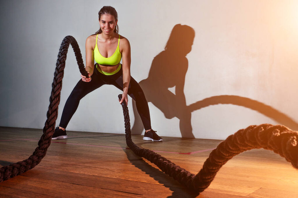 young woman in green sports bra and black pants is trained with the help of ropes in the gym - Zdjęcie, obraz