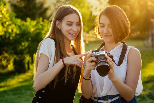 two female friends in the park photographing on a professional camera . photo shoot photosession in the city - Foto, imagen