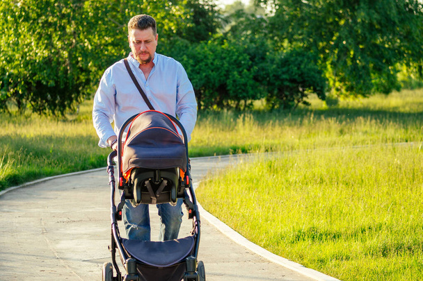 handsome man is walking with a baby in a stroller in the park - Foto, Bild