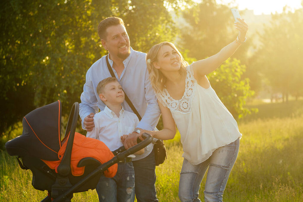 aktywne duży szczęśliwy rodzina ojciec, matka, syn i dziecko w wózku spacerowym w parku są fotografowane na telefon selfie - Zdjęcie, obraz