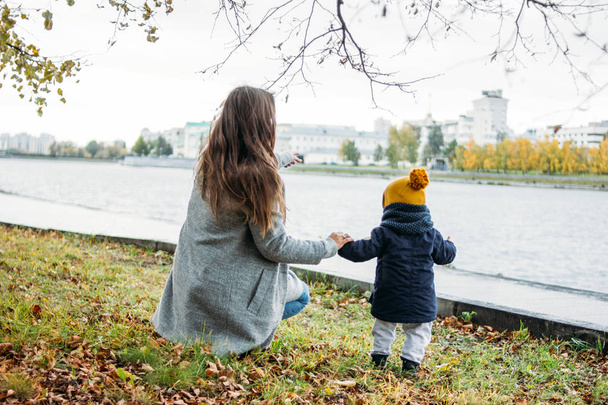 Lindo bebé niño en ropa casual de moda explora el mundo con la madre en el parque natural de otoño, la gente por detrás
 - Foto, Imagen