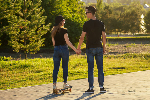 active couple in love sport skating in the summer park. beautiful woman and man have fun with skateboard longboard background the river. guy and girl date. active lifestyle among young people - Photo, Image