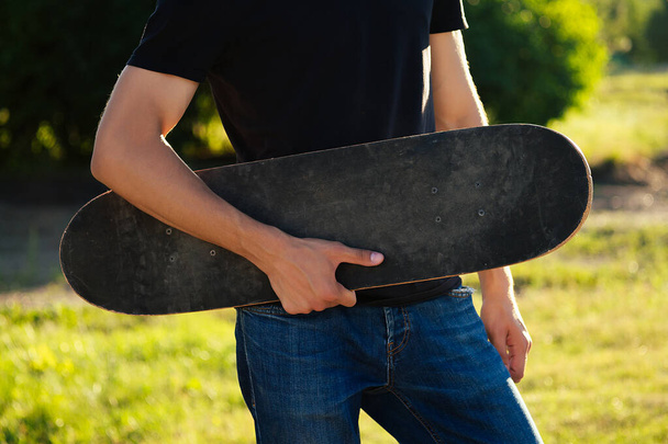 skateboard longboard close-up in the hands of a young man in jeans and a black T-shirt in the park - Fotoğraf, Görsel