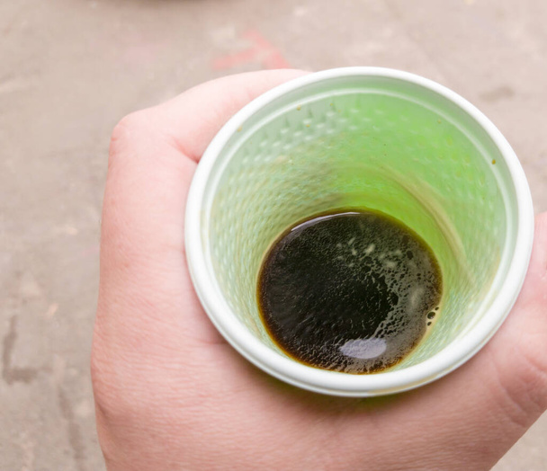 grüne Plastikbecher mit schwarzem Kaffee in der Hand eines Mannes im Freien. Ein Mann hält ein Glas Kaffee in der Hand. Blick von oben. - Foto, Bild