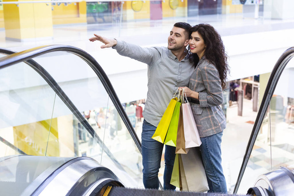 Šťastný mladý pár s nákupními taškami stoupá na eskalátoru - Fotografie, Obrázek