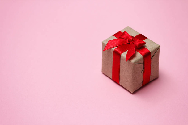 Gift box wrapped in brown craft paper and tie red satin ribbon. Pink solid background. Sale concept. Long horizontal banner photo format. Your text space.  - Photo, image
