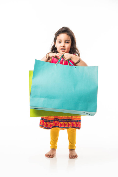 Ινδικό μικρό κορίτσι κρατώντας τσάντες ψώνια, στέκεται απομονωμένο πάνω από λευκό φόντο - Φωτογραφία, εικόνα