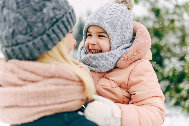 Rear view close-up portrait of happy little girl smiling and playing together with her mother in the park on snowing day. Beautiful woman and her child walking on winter day. Christmas mood. Childhood - Φωτογραφία, εικόνα