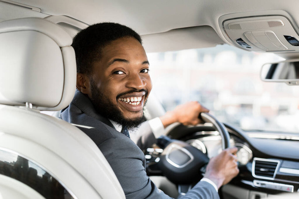 Молодой афро-бизнесмен на водительском сидении улыбается в камеру
 - Фото, изображение