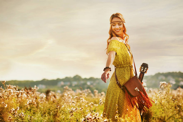 dziewczyna w żółtym stylu sukienka bohemian, trzymając gitarę na polu z ciepłą i komfortową atmosferę zachód słońca - Zdjęcie, obraz