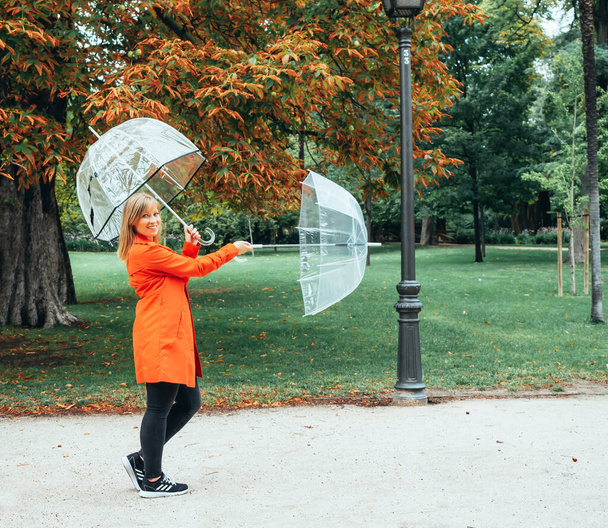 fille caucasienne en gabardine rouge joue avec deux parapluies transparents dans un parc
 - Photo, image