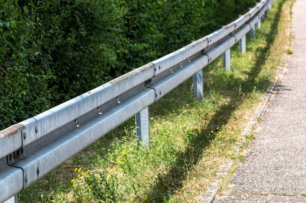 Crash barrière bij de straat met struiken, gras en asfalt - Foto, afbeelding