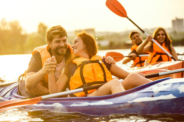 Happy friends kayaking on river with sunset on the background - Фото, изображение
