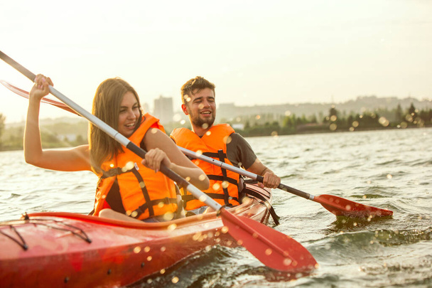 Happy couple kayaking on river with sunset on the background - Photo, Image