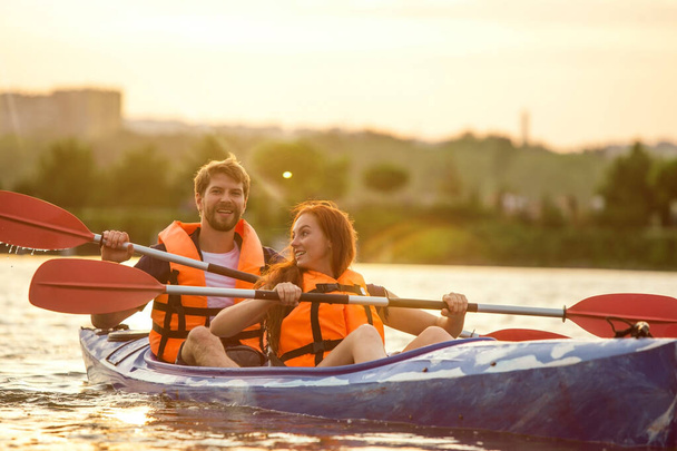 Happy couple kayaking on river with sunset on the background - Foto, Imagem
