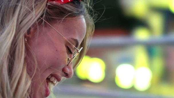 Vista lateral cortada de atraente jovem loira sorrindo e rindo ao usar o smartphone no parque de diversões
 - Filmagem, Vídeo