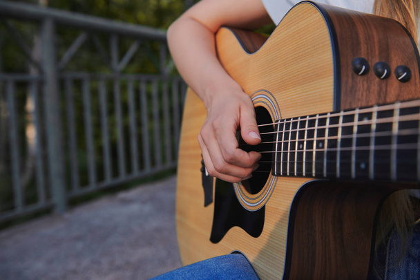 Holčičí ruka hraje na akustickou kytaru. Mladý hudebník vydělává na mostě. Pouliční hudební koncept. Closeup. - Fotografie, Obrázek