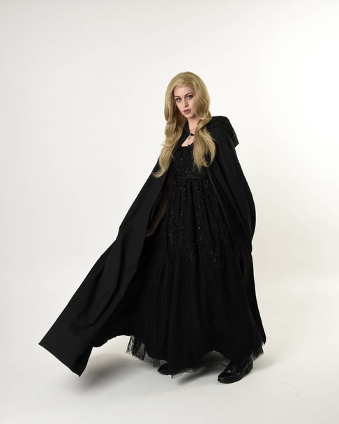 retrato de comprimento total de menina loira vestindo manto longo fluxo preto, em pé posar com um fundo de estúdio branco
. - Foto, Imagem