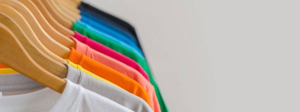 Крупный план красочных футболок на вешалках, на фоне одежды
 - Фото, изображение