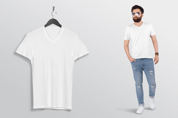 ブルーデニムジーンズパンツで男性モデルと壁に無地の白いvネックTシャツをぶら下げて。隔離された背景.  - 写真・画像