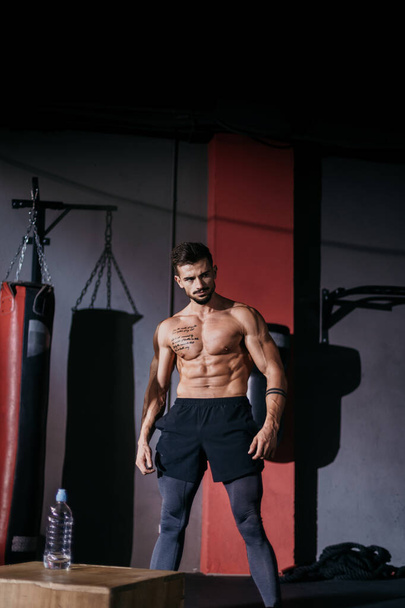 Πορτρέτο άνθρωπος bodybuilding στέκεται μπροστά από την κάμερα και θέτοντας σε μια κλάση γυμναστήριο με μαύρο φόντο - Φωτογραφία, εικόνα