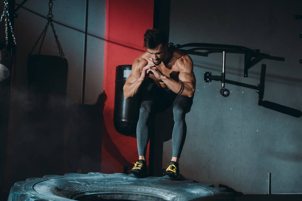 Fit μυώδης άνθρωπος κάνει cross Fit ασκήσεις κάνει push ups πάνω από το ένα μεγάλο ελαστικό ελαστικό σε μια τάξη γυμναστήριο αυτός να γλυταίνει πολύ συγκεντρωμένη εργασίας έντονη - Φωτογραφία, εικόνα