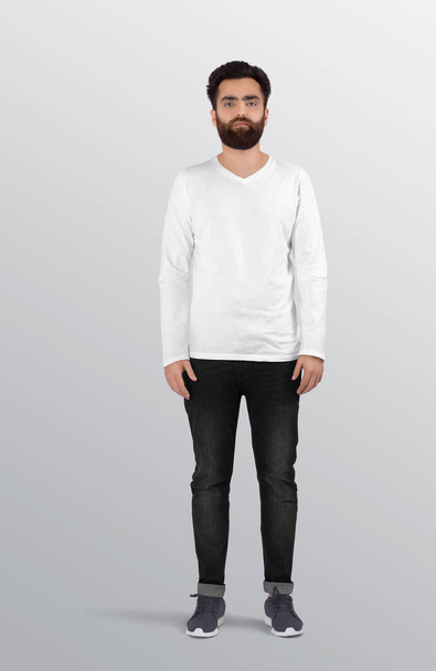 Staande reu model met effen wit v hals shirt met lange mouwen in zwarte denim jeans broek. Geïsoleerde achtergrond - Foto, afbeelding