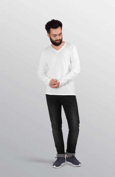 Μόνιμη αρσενικό μοντέλο φορώντας απλό λευκό v λαιμό μακρύ μανίκι πουκάμισο σε μαύρο τζιν παντελόνι. Μεμονωμένο φόντο - Φωτογραφία, εικόνα