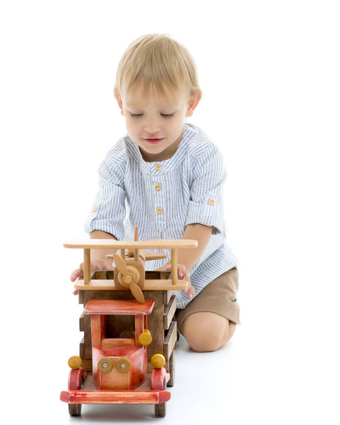 Μικρό αγόρι παίζει με ένα ξύλινο αυτοκίνητο. - Φωτογραφία, εικόνα